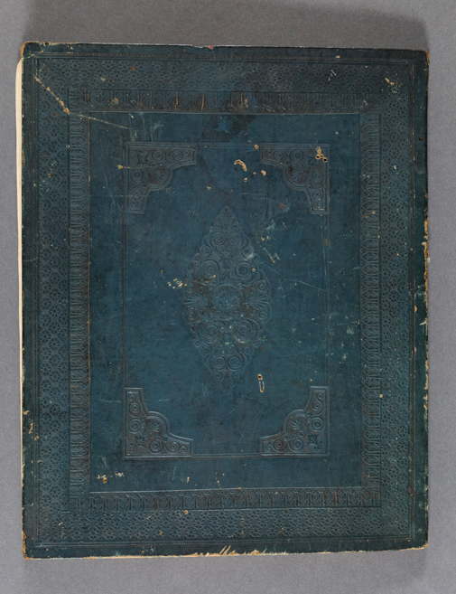 Esta imagem é uma foto da capa de uma caderneta. A fotografia apresenta a capa anterior de caderneta de Félix-Émile Taunay, irmão de Aimé-Adrien Taunay, na cor azul. O objeto possui aparência de desgaste e detalhes abstratos em voluta em baixo relevo separadas por molduras também em relevo.